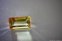 Angle showing rectangular cut natural yellow sapphire gemstone with reflective facets and yellow hue.