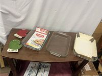 Photo shows three clear glass Pyrex baking dishes on wooden table with two mitten-shaped spoon rests, one red and one green with holly detail.