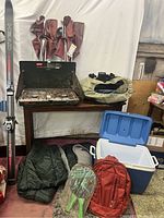 Full view of camping lot items including sleeping bags, propane stove, cooler, backpack, paddleball set, chairs, and skis.