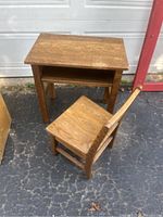 Small wooden desk and matching chair on asphalt floor outside.