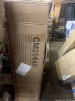 Photo shows the boxed packaging of the Costway Christmas tree with model number CM20640 visible on the box, stored in a warehouse environment.