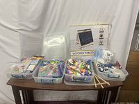 Photo of three plastic containers filled with colorful kids craft supplies and a boxed wooden tablet on a table