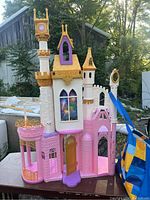 Front view showing detailed windows with princess images, multiple turrets with gold crowns on top, a balcony area with railings, and an open front door.