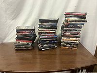 Three stacks of assorted DVD movies on a wooden table against a white fabric background.