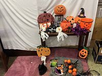 Full view of Halloween decorations including various pumpkin buckets, ghost figures, witch hat, purple wreath, and assorted items on and below a small table.