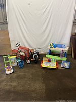 Full view of all items showing the vintage tractor, tricycle, electronic toy, play table with helmet, bucket and chalk