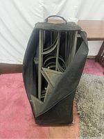 Metal frame parts and perforated panels packed inside a large black carrying bag with handles, sitting on carpet.