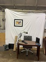Desk with office chair, desk lamp, computer monitor, framed artwork on white backdrop