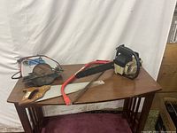 Photo showing the four saws on a wooden table with white sheet background: circular saw, gas chainsaw, handsaw, and branch saw