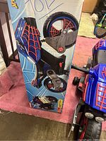 Photo showing the motorcycle and its original box with Spider-Man branding and blue background.