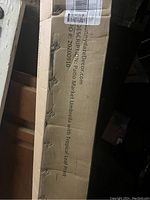 Box showing product labeling as Sunnydaze Patio Market Umbrella with Tropical Leaf Print.