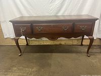Front view of the wooden Thomas table showing three drawers, scalloped apron, and cabriole legs.