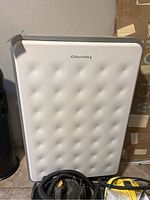 Front view of white Coway air purifier with tufted front panel and power cord visible below.