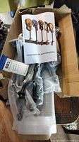 Contents of cardboard box showing black metal parts of the guitar rack and instruction manual with images of 5 guitars in the rack.