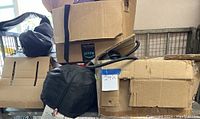 Full cart view with multiple cardboard boxes stacked, visible sticker with number 242, black tent bag, coiled cables, and packaging materials.