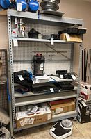 Front view of the metal shelving unit showing four shelves with various items on them (not included in sale) and pegboard backing.
