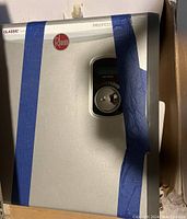 Front view of Rheem unit in box with blue tape across casing
