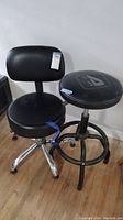 Two black seating items, one adjustable rolling chair with backrest and casters, one adjustable padded stool with foot ring.