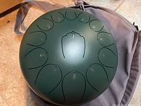 Image of green steel tongue drum placed on grey carrying bag highlighting numbered tongue keys.