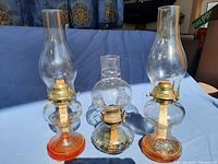 Front view of three vintage oil lamps, showing two matching lamps with orange glass bases and one single lamp with a clear base.