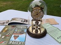 Full clock under glass dome on wooden base with original papers spread behind on table.
