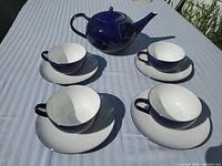 Teapot with four matching cups and saucers on a white tablecloth under natural light