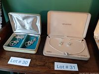 Two Vendome jewelry sets in original cases: a necklace and earring set on the right with a white case, and a different set on the left with blue velvet lining in a white and gold case.