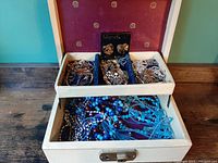 Overall view of the box showing top and bottom compartments, assorted metallic bracelets, chains, and blue beaded jewelry inside