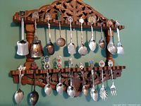 Photo shows the full wooden carved rack holding 20 unique collector spoons and one fork. Spoons vary in handle design and bowl shape or decoration.