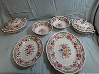 Full set comprising 2 lidded serving dishes, 2 bowls, and 2 serving platters showing floral pattern and scalloped edges.
