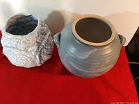 Two vintage pottery pieces side by side: left is a textured blue cabbage design vase, right is a round vintage pottery vase with handles and smooth glaze, all on red cloth.