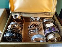 Vintage hinged bangle bracelets collection in vintage jewelry box, showing multiple bracelets of varying designs and colors