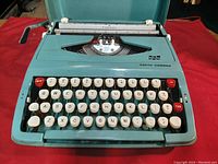 Front view showing keyboard layout with cream colored keys and red shift and tab keys, teal body, and Smith Corona branding.