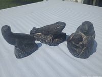 Three dark soapstone aquatic animal sculptures: sea lion, harbor seal, beaver family.