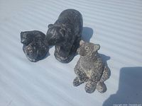 Overview of three soapstone bear figures including one large adult and two cubs on a white fabric surface under natural light.