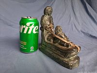 Side view of green soapstone carving showing woman standing behind child on sleigh with soda can for scale.