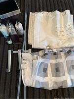 Photo of two shower curtains folded, metal curtain rods, and over door hooks on a carpeted floor.