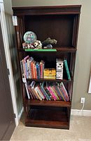 Front view of the dark wooden bookcase filled with books on the middle and lower shelves and decorative items on the upper shelf.