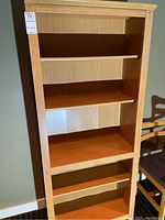 Full front view of the laminate bookshelf showing five shelves and light wood grain finish.