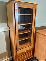 Full view of the tall wood and laminate cabinet, showing glass door and drawers with wooden knobs.