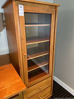 Front view of tall wood laminate cabinet with glass door revealing interior shelves and two lower drawers