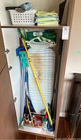 Full view of closet with ironing board, cleaning tools including broom, mop, spray bottles, and storage basket