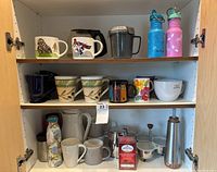 Shelf with various coffee mugs, two insulated water bottles on the top shelf, a coffee press, pitchers, and coffee accessories arranged on lower shelves.
