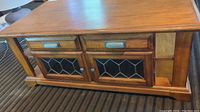 Front view of the coffee table showing the two small drawers above leaded glass cabinet doors and open shelving on the sides.