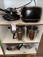 Shelf with cookware stacked including frypans, stainless steel pots, and the toaster