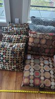 Photo showing five cushions: three with small multicolor circles on black, two with gray and white geometric diamond pattern.