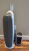 Honeywell upright tower fan and Bionaire smaller tower fan positioned side by side on floor against wall.