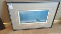 Front view of the framed artwork featuring lighthouse on island in blue tones.