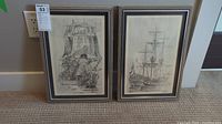 Pair of framed sailing ship artworks leaning against a wall on floor. Both frames light wood and artwork in black and white.