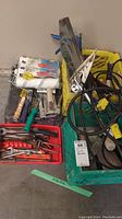 Overview of the hardware and tools in crates including extension cords, paint rollers, putty knives, and hand tools on concrete floor